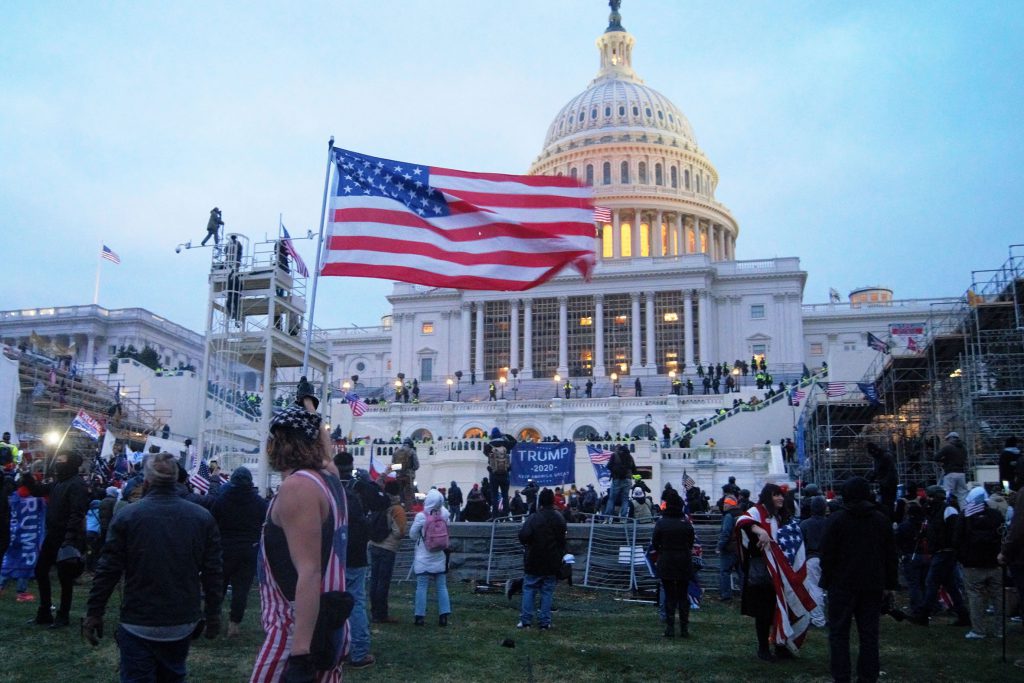 Fotografia colorida que mostra pessoas em uma manifestação antidemocrática nos Estados Unidos. Ao fundo, o prédio do Capitólio.