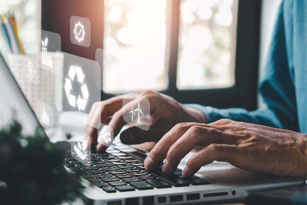 Fotografia colorida que mostra uma pessoa digitando em um notebook. Sobrepostos à foto, ícones que simbolizam o meio ambiente e a sustentabilidade.