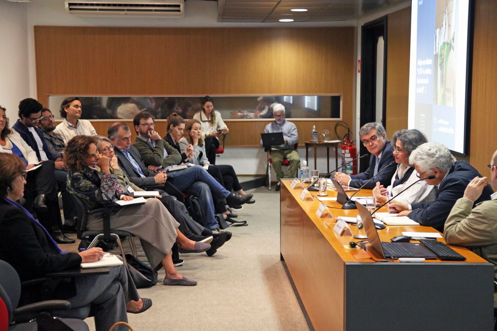 Fotografia colorida que mostra o evento realizado no auditório da Fundação FHC. À direita, atrás de uma mesa de madeira, estão os quatro palestrantes. À esquerda, a plateia.