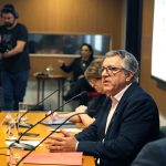 Fotografia colorida de um debate no auditório da Fundação FHC. À direita, atrás de uma mesa de madeira, os palestrantes. Todos estão sentados. Sobre a mesa, microfones. Um homem está falando. Ele olha para a plateia, que está à frente. 