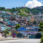 Fotografia colorida de uma cidade na Venezuela. Em primeiro plano, uma rua que leva até um túnel. Ao fundo e sobre o túnel, diversas casas coloridas em um morro.