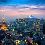 Fotografia colorida que mostra uma cidade do Japão. Em primeiro plano, diversos prédios modernos. Ao fundo, o monte Fuji.