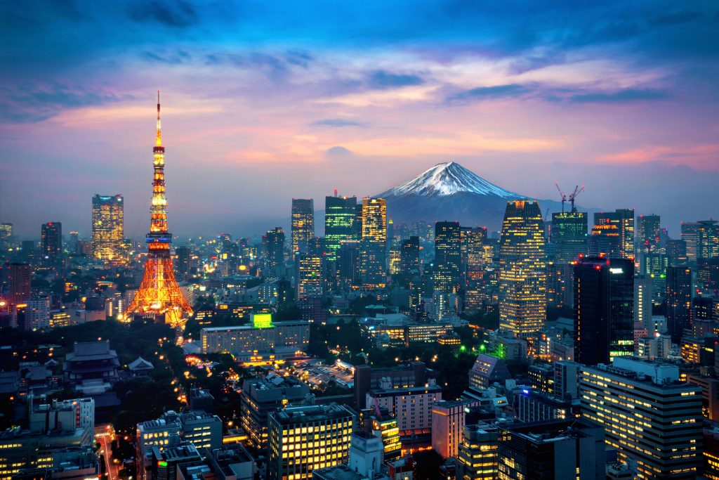 Fotografia colorida que mostra uma cidade do Japão. Em primeiro plano, diversos prédios modernos. Ao fundo, o monte Fuji.