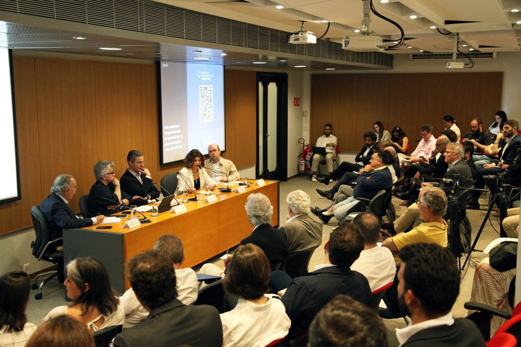 Fotografia colorida de um debate na Fundação FHC. À direita, a plateia. Todas as pessoas estão sentadas. À esquerda, sentados atrás de uma mesa de madeira, os palestrantes. Uma mulher está falando. Sobre a mesa, um microfone.