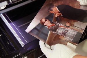 Fotografia colorida que mostra uma foto do Acervo da Fundação FHC que será digitalizada em uma máquina. A foto é colorida e mostra a atriz Fernanda Montenegro e o presidente Fernando Henrique Cardoso.